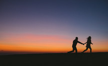 the silhouette of a couple running holding hands at sunset 