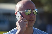 a man having a cellphone conversation with reflection in his sunglasses 