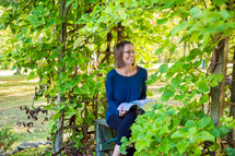 a woman sitting on a bench reading outdoors 