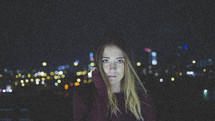 stoic face of a woman standing in a city at night 