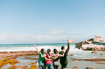 friends standing on a shore with raised hands 