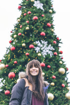 a smiling young woman standing in front of a Christmas tree 
