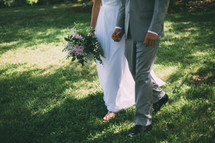 bride and groom holding hands walking through grass