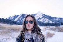 A young woman in sunglasses standing in front of a snow capped mountain 