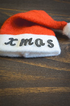 A little Santa hat with the letters Xmas on it. On a wooden background. background for Christmas.