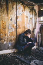 A woman sits sits in an abandoned house with her head in her hands.