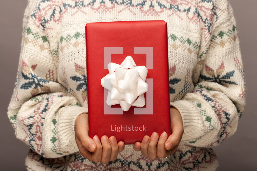 a woman in a sweater holding a wrapped Christmas gift 
