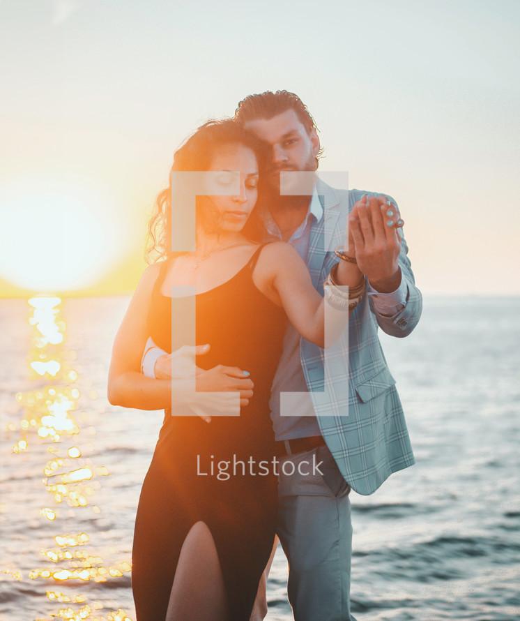 Energetic attractive young couple dancing latin Bachata near sea or ocean. Sunlight background. Summer time, romantic 
