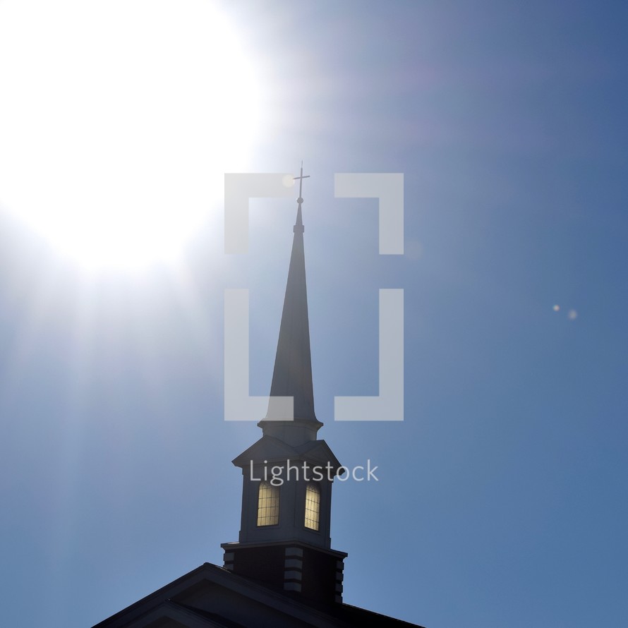 glowing sun over a steeple against a blue sky 