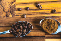 Spoons with coffee powder and coffee beans, laying down on a wooden background.