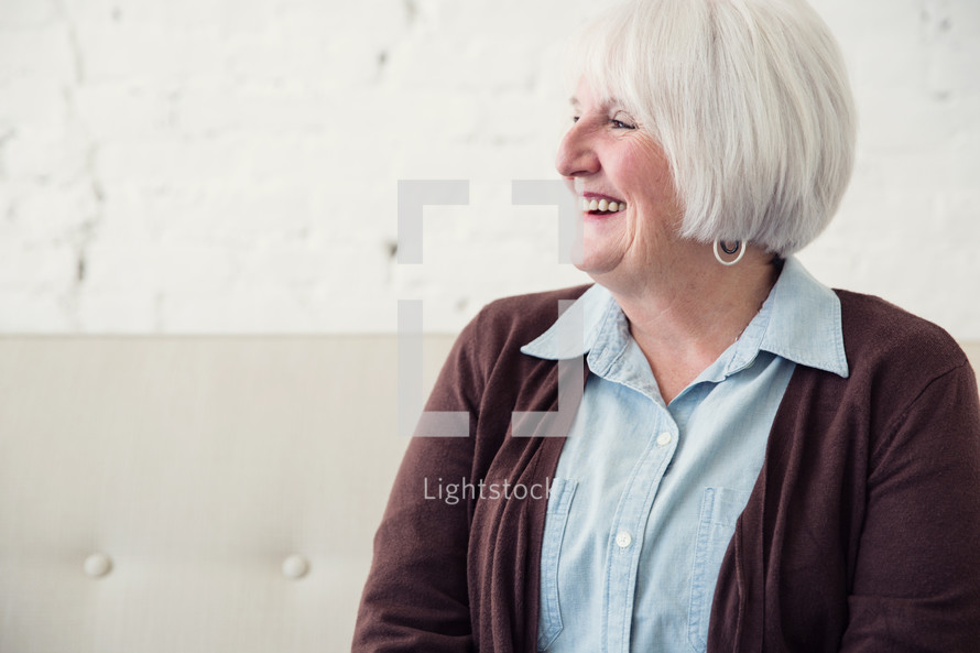 a mature woman sitting on a couch laughing.