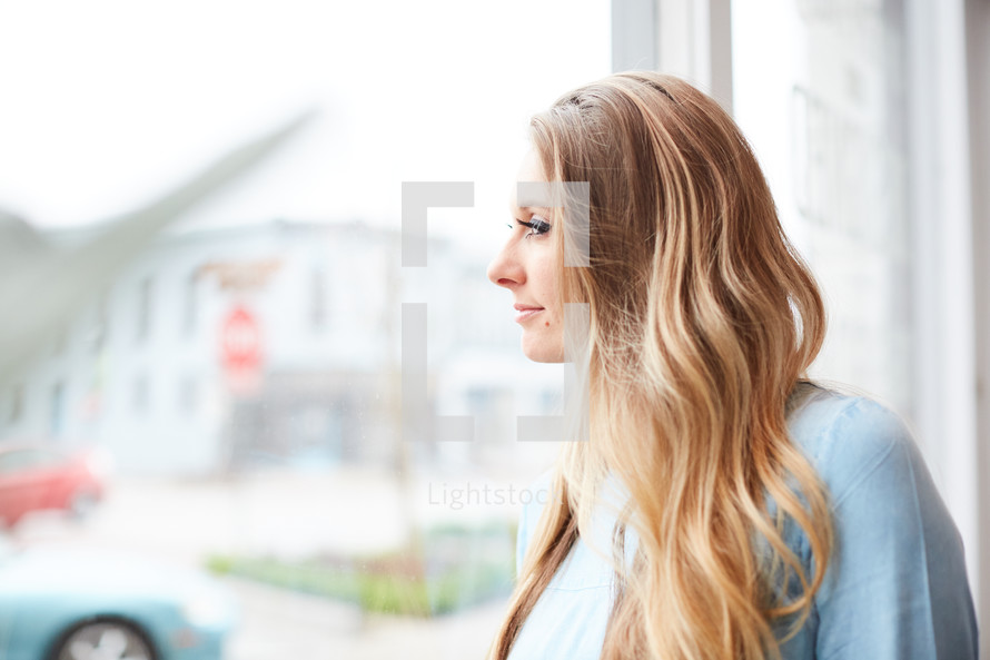 a young woman standing in front of a window daydreaming 