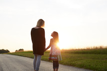 a mother and daughter standing together outdoors at sunset 