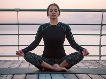 Peaceful yogi woman sitting in lotus meditating, feeling free in front of sea. Mindful fitness coach having zen moment. Everyday yoga practice, calm breath, concentration concept