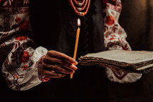 Ukrainian woman reading ancient book - Bible. Concentrated follows finger on paper page under candle light. History of Kyiv Rus. Psalter, 19th century, prayers and psalms.