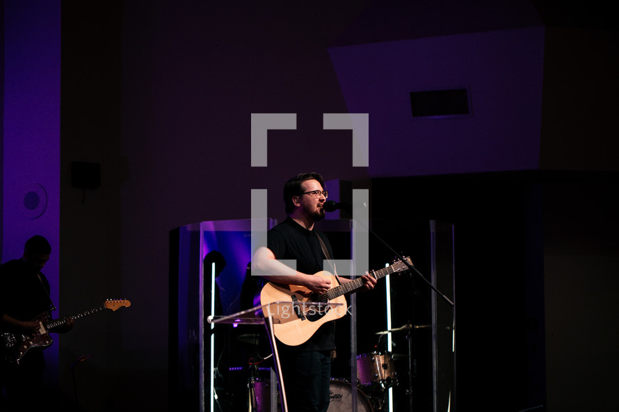 a man singing with a guitar during a worship service 