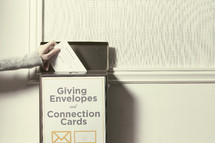 Hand placing an envelope in the donation box.