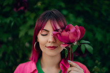 Portrait of real serene woman with vivid dyed pink fuchsia hairstyle. Peony flower, green nature backdrop. Trendy colorful hair, stylish haircut