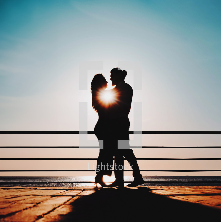 Silhouette of young attractive couple dancing latin bachata near sea or ocean. Sunlight background. Summer time, romantic