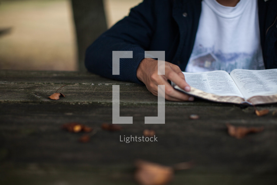 torso of a young man reading a Bible outdoors 