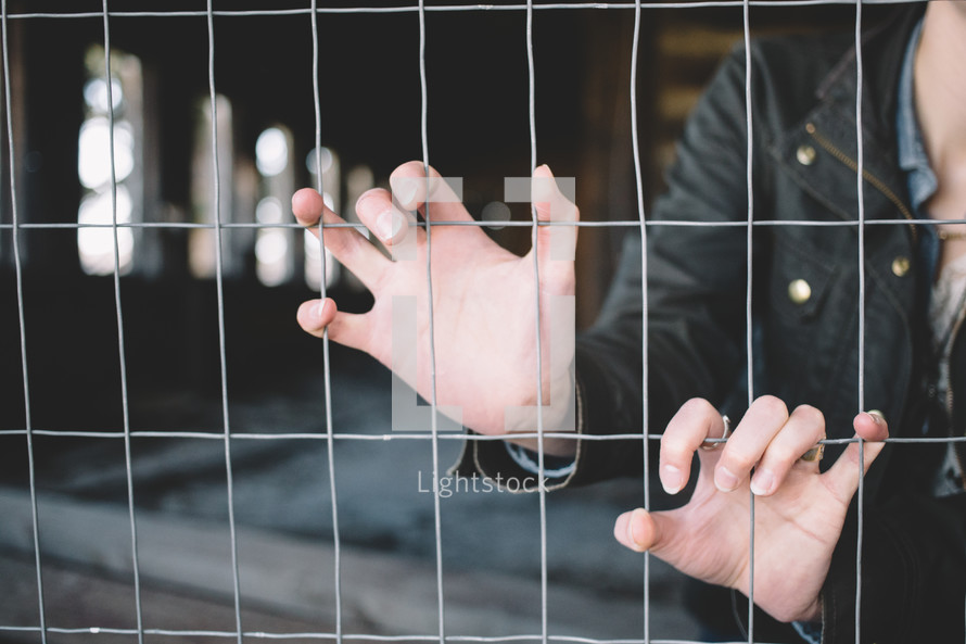 A woman's hands grasp a wire fence.