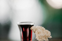 communion wine in a cup and bread against a bokeh background 