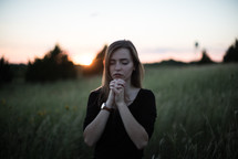 a woman in a field praying reverently 