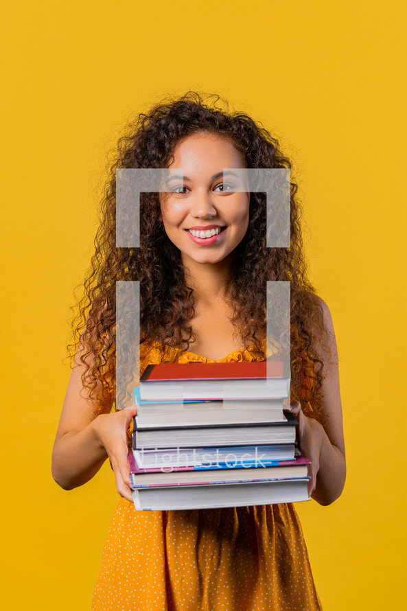 Adult happy student woman with stack of books from library on yellow background. Happy girl smiles, she is happy to graduate. High quality
