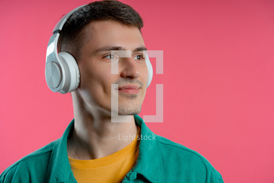 Positive man listening music, enjoying dance with headphones on pink studio background. Radio, wireless modern sound technology, online player. High quality photo