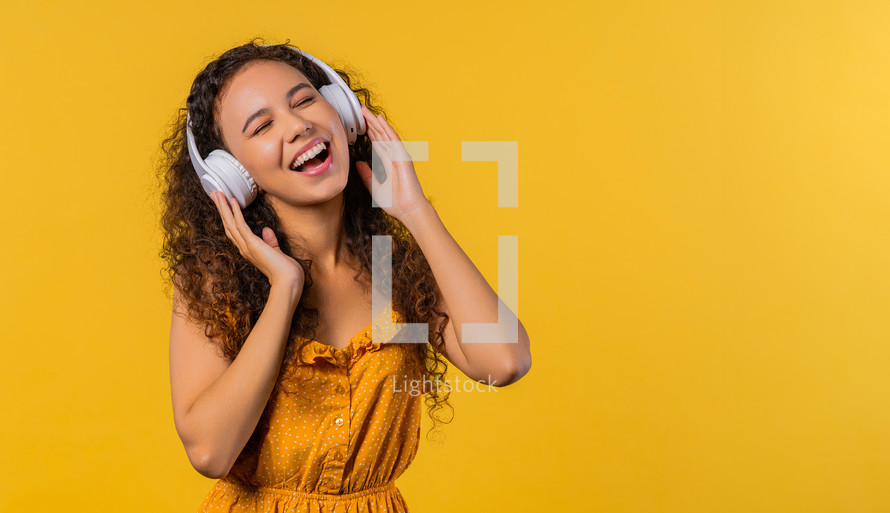 Positive woman listening music, enjoying with headphones on yellow studio background. Radio, wireless modern sound technology, online player. High quality photo