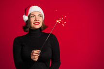 Trendy hipster girl in Santa hat with bengal sparkler fire on red background.
