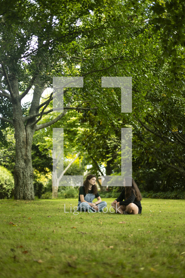 two young women sitting together talking in the grass in a beautiful setting