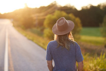 a woman in a hat walking down a rural road 