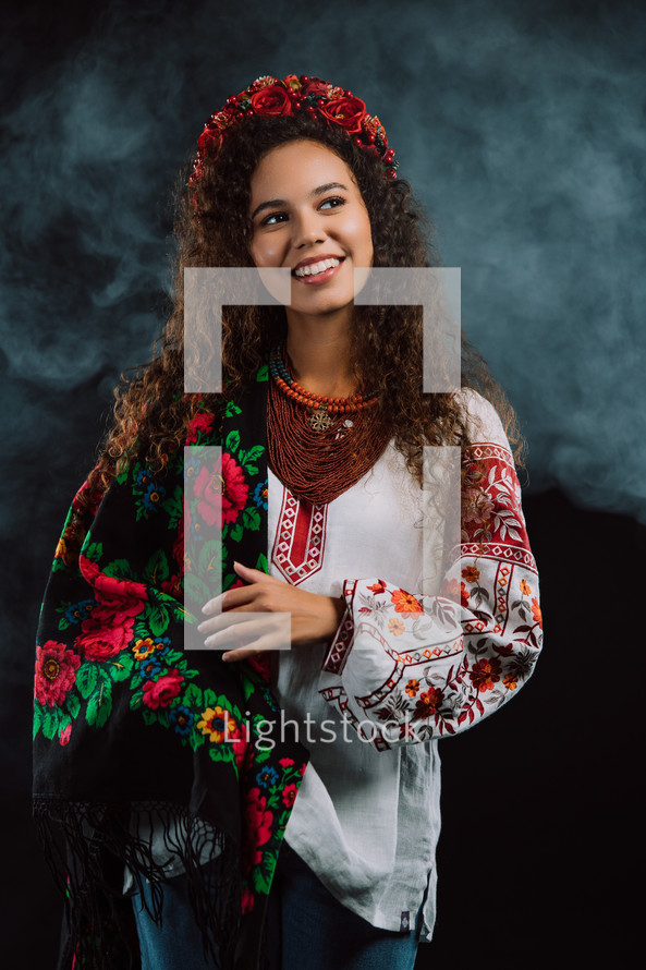 Modern young woman in traditional ukrainian handkerchief, necklace and embroidered blouse at multi-colors neon light smoke background. Ukraine, style, folk, culture. High quality photo