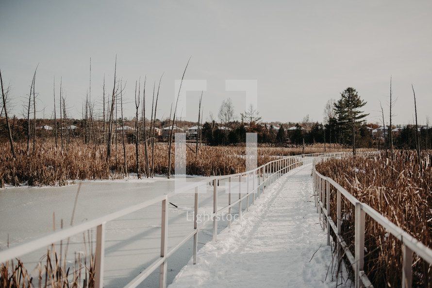 snow on a boardwalk over a pond 