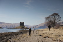 a castle and people walking along a lake shore 
