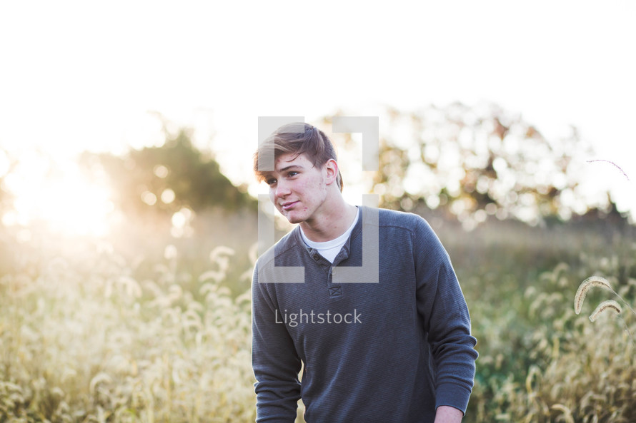 a young man walking through a field of tall grass 