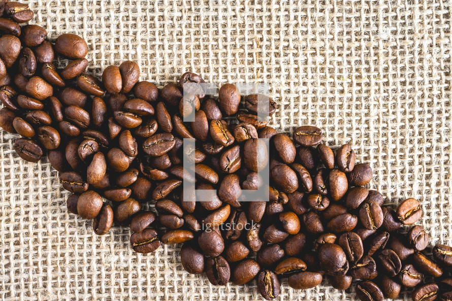 Bunch of Coffee beans laying on burlap fabric. Background voor coffee related products.