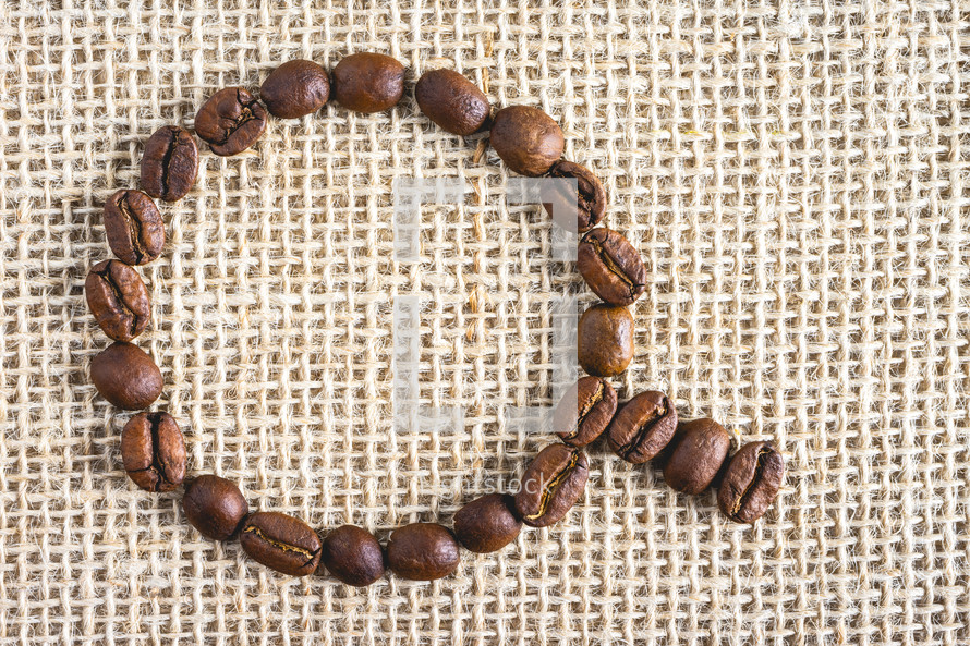 Coffee beans in the shape of a cup, on a burlap fabric. Background voor coffee related products.
