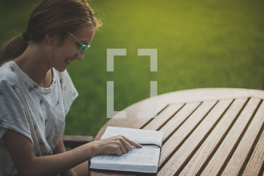 a young woman reading a Bible in her backyard 
