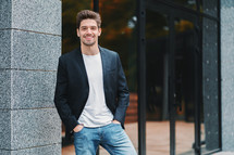 Portrait of young successful confident businessman in the city on office building background. Man in business suit looking to camera and smiling. Portraiture of handsome guy.