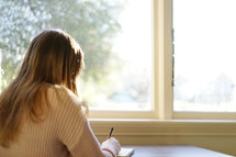 woman writing in a journal in front of a window 