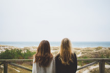 two women looking over a railing at a beach