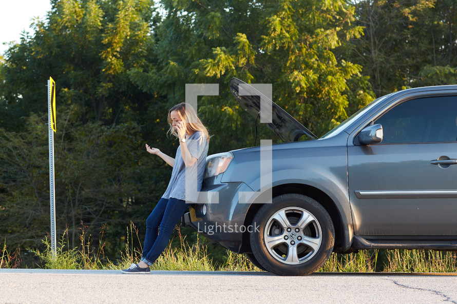 a woman on the phone next to a broken down vehicle 