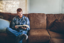 man reading a Bible while sitting on a couch