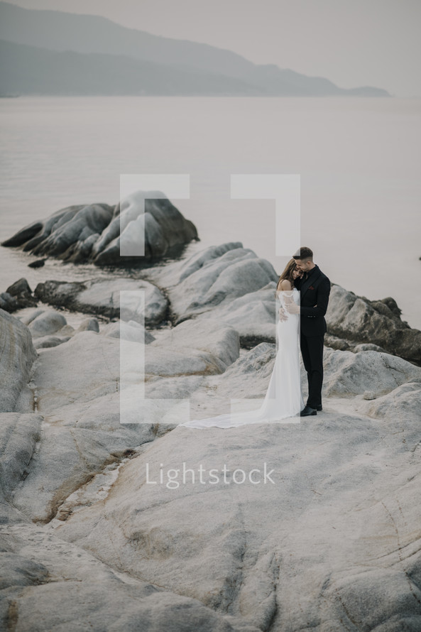 bride and groom standing on a rocky shore 