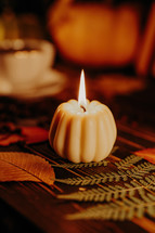 Autumn background. Pumpkin candle, orange fallen leaves. Flat lay. Cozy ambiance of fall, candle burning. Seasonal promotions or tranquil visual storytelling. 