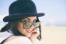 Portrait of smiling beautiful young woman in black hat retro sunglasses on beach