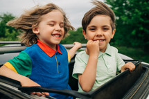 Adorable happy little kids stands in open car sunroof during road trip in countryside at summer. Concept of family leisure, active traveling. High quality photo. 