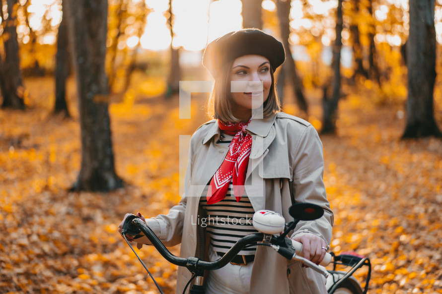 Young pretty woman riding vintage white bicycle in autumn park. Lady having fun on orange nature fall background. High quality photo